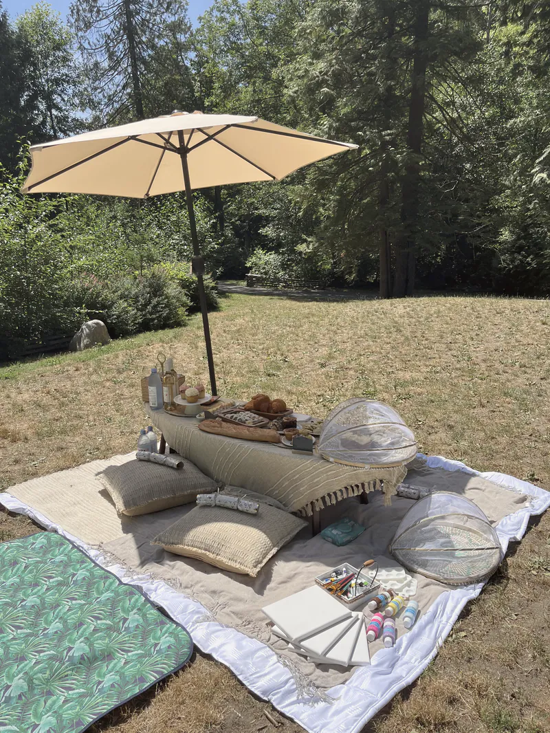 An outdoor picnic under a linen umbrella with cushions and blankets